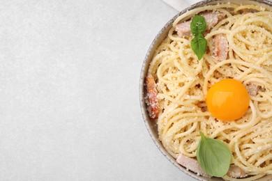 Photo of Bowl of tasty pasta Carbonara with egg yolk on light grey table, top view. Space for text