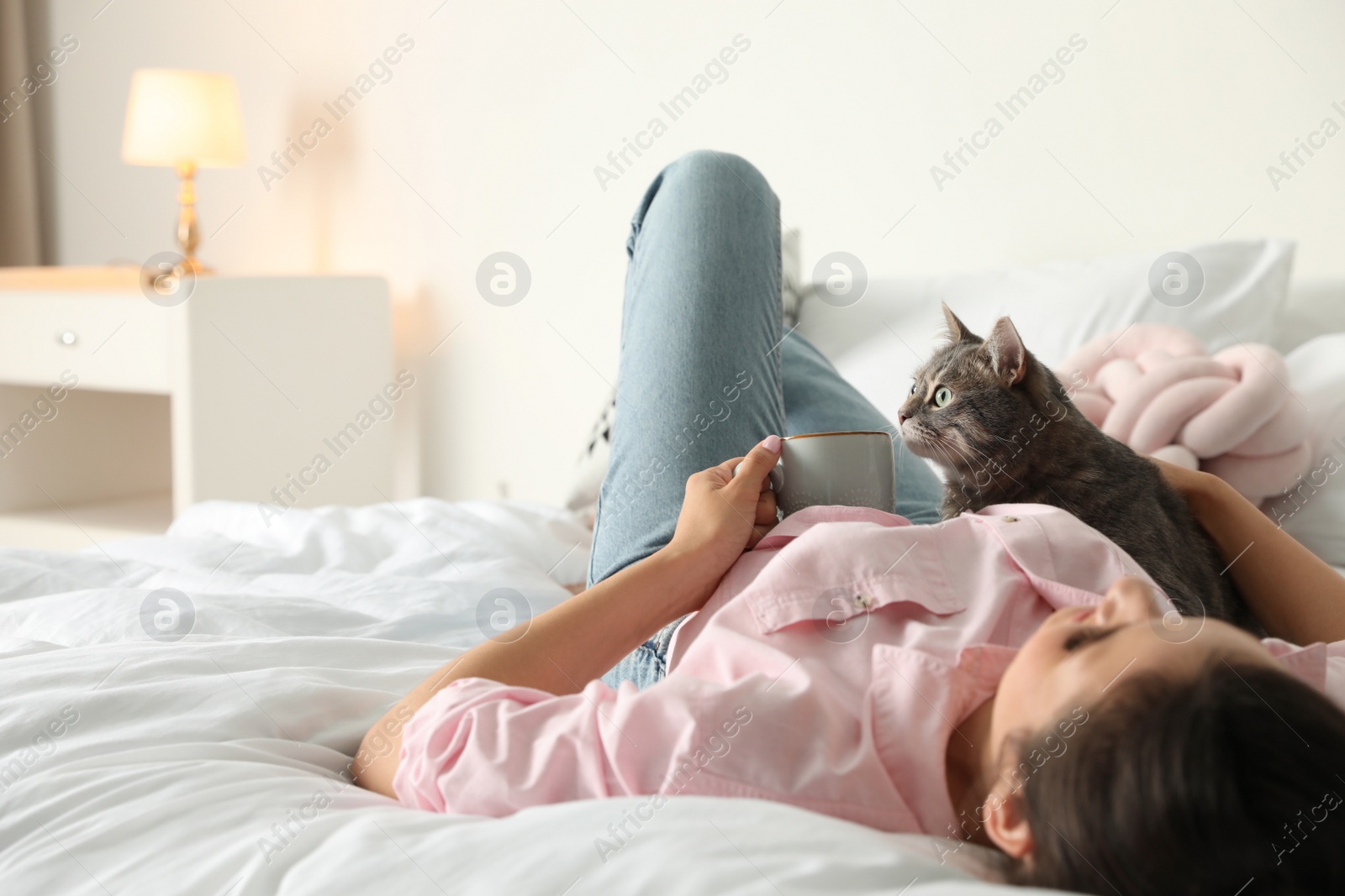 Photo of Young woman with cute cat on bed at home, space for text. Pet and owner