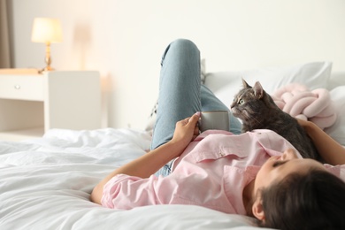 Young woman with cute cat on bed at home, space for text. Pet and owner