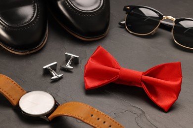 Photo of Stylish red bow tie, sunglasses, shoes, wristwatch and cufflinks on grey background