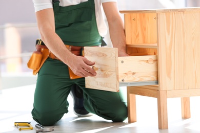 Photo of Handyman in uniform assembling furniture indoors, closeup. Professional construction tools