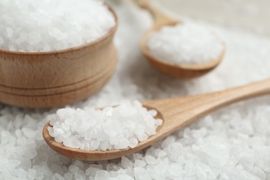 Photo of Pile of natural sea salt with wooden bowl and spoons, closeup