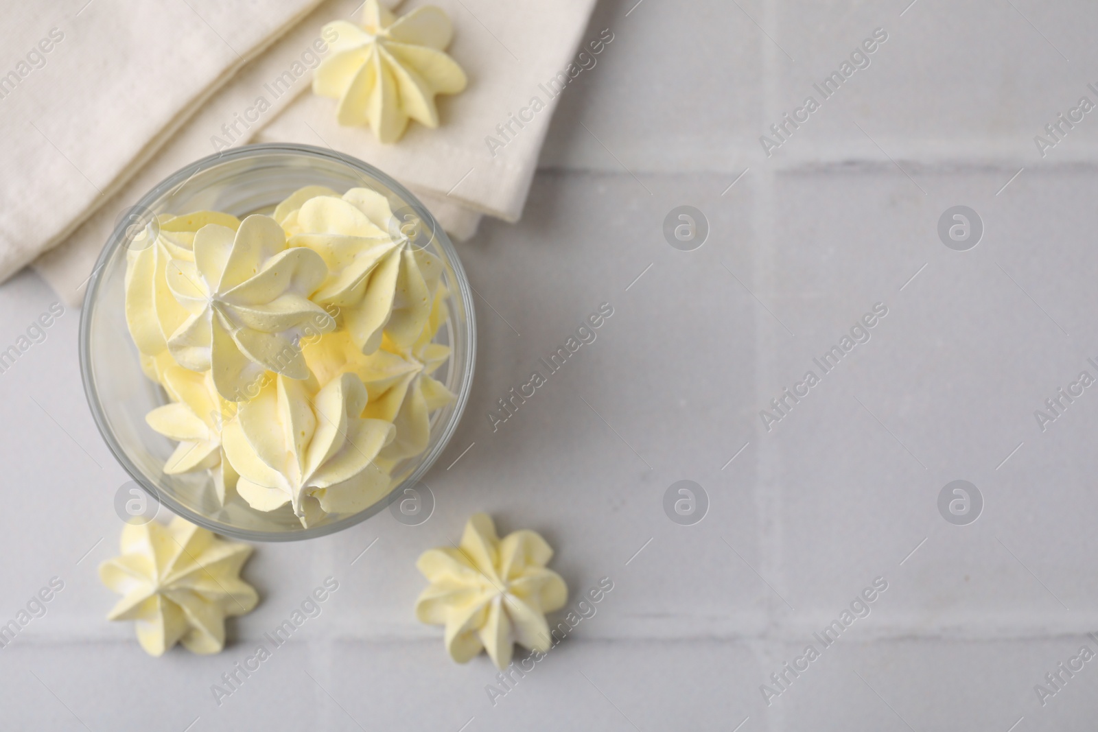 Photo of Tasty meringue cookies in glass on white tiled table, top view. Space for text