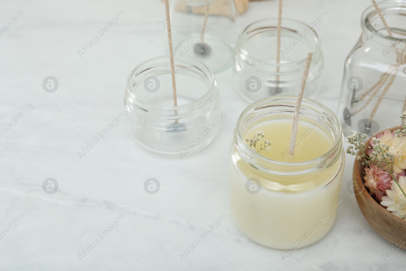 Photo of Glass jar with wax, wick and flowers on white table, space for text. Making homemade candle