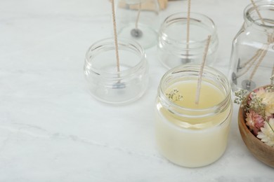 Glass jar with wax, wick and flowers on white table, space for text. Making homemade candle