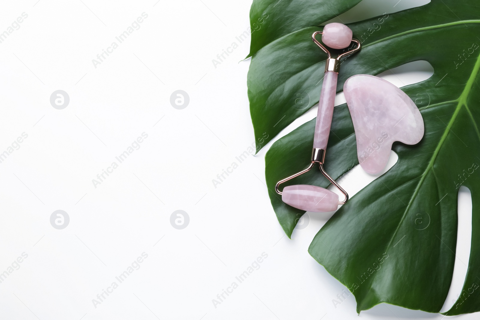 Photo of Gua sha stone, face roller and monstera leaf on white background, flat lay. Space for text