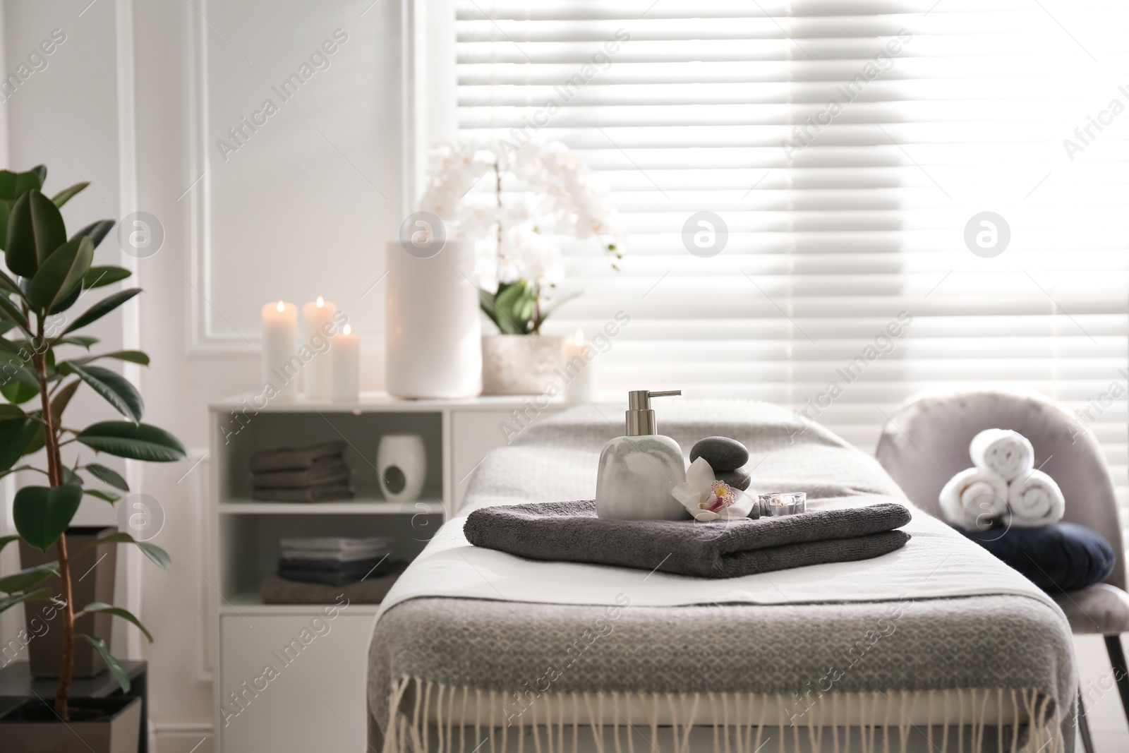 Photo of Dispenser, candle and orchid flower on couch in spa salon