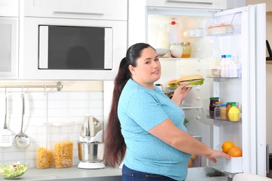 Overweight woman taking sandwich from refrigerator in kitchen. Failed diet
