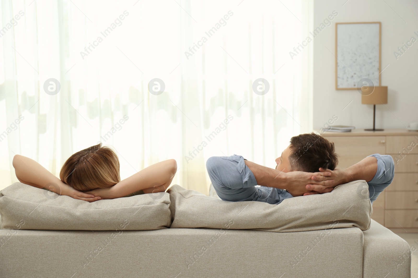 Photo of Couple relaxing on sofa in living room, back view