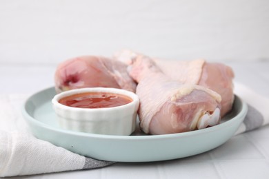 Fresh marinade and raw chicken drumsticks on white tiled table, closeup