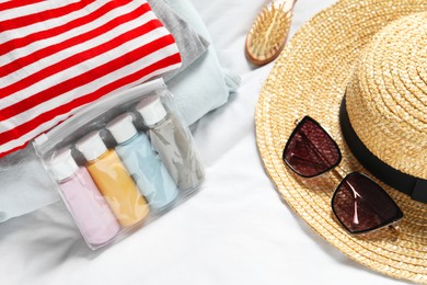 Photo of Cosmetic travel kit. Plastic bag with small containers of personal care products, beach accessories and stack of clothes on bed