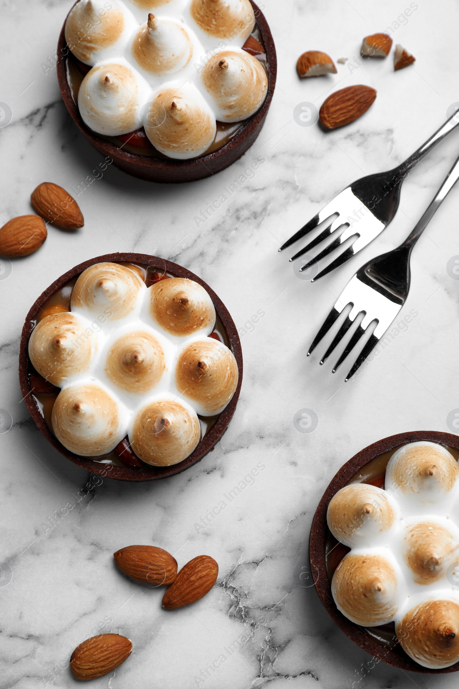Photo of Delicious salted caramel chocolate tarts with meringue and almonds on white marble table, flat lay