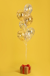 Bright balloons and gift box on color background