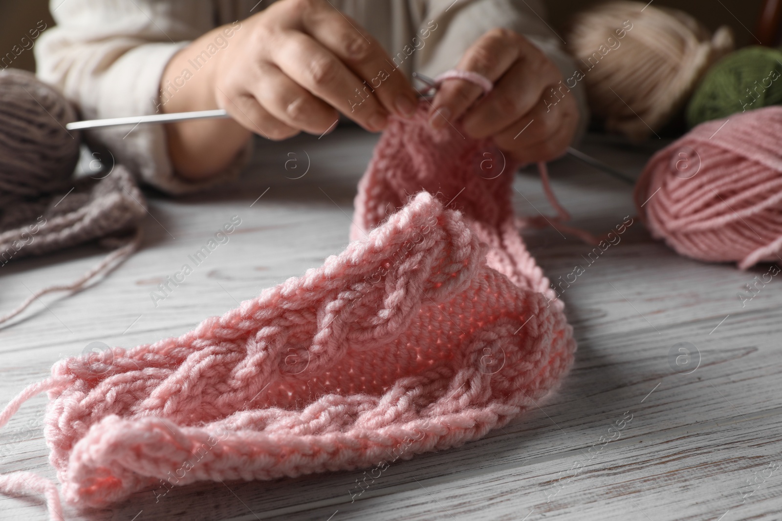 Photo of Woman knitting at white wooden table, closeup. Creative hobby