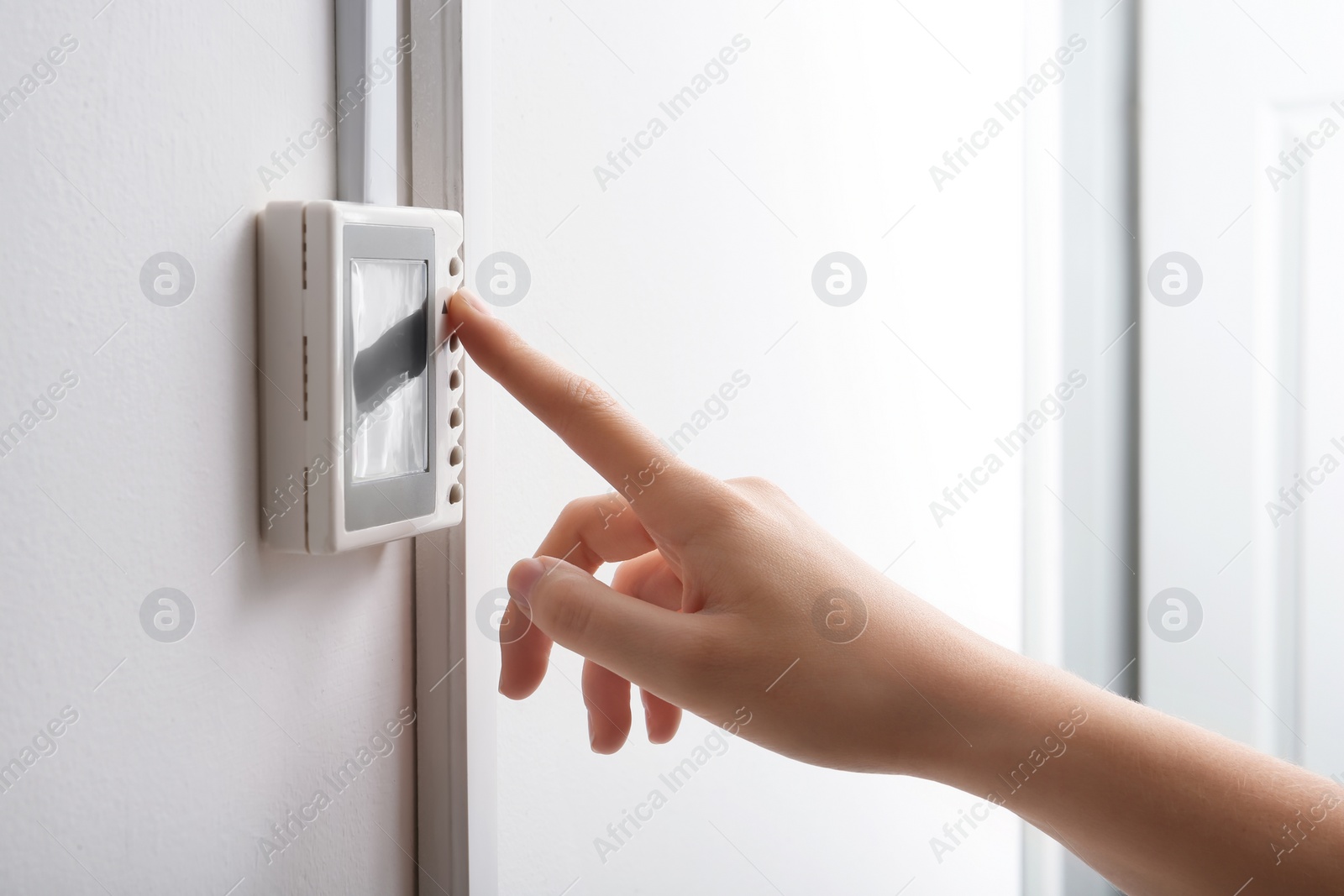 Photo of Woman adjusting thermostat on white wall, closeup. Heating system