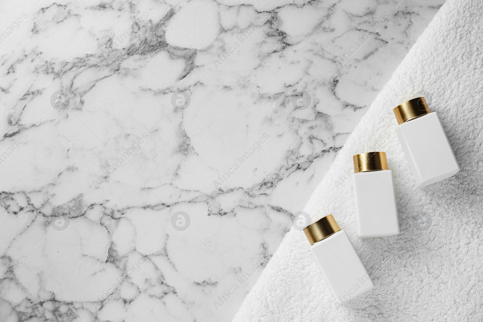 Photo of Cosmetic bottles and fresh towel on marble table, top view with space for text. Spa treatment