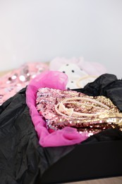 Headbands and stylish pink carnival costume with sequins in black box on wooden table, closeup