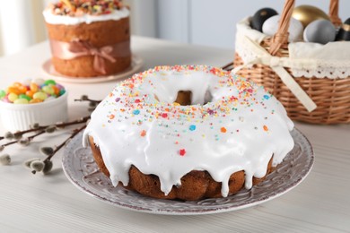 Photo of Delicious Easter cake decorated with sprinkles near willow branches, candies and painted eggs on white wooden table
