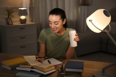 Photo of Young woman with energy drink studying at home