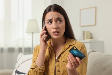 Photo of Confused woman with credit card talking on phone at home. Be careful - fraud