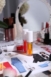 Photo of Bright lip glosses among different cosmetic products and fashion magazine on table indoors