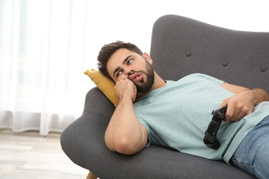 Photo of Lazy young man playing video game while lying on sofa at home