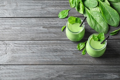 Jars of healthy green smoothie with fresh spinach on grey wooden table, above view. Space for text