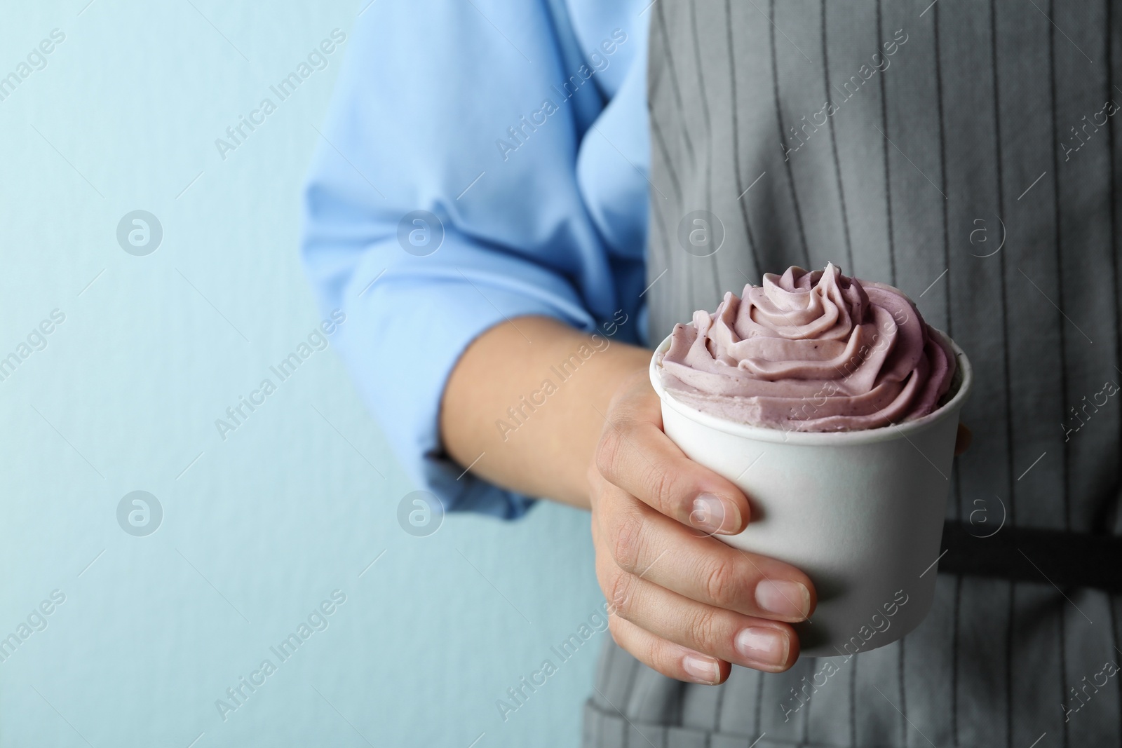 Photo of Woman holding cup with tasty frozen yogurt on blue background, closeup