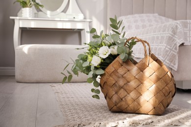 Photo of Stylish wicker basket with bouquet on floor in bedroom, space for text