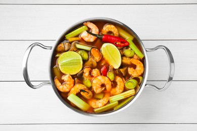 Photo of Saucepan with delicious Tom Yum soup on white wooden table, top view