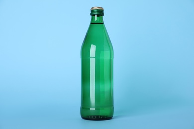 Glass bottle with water on light blue background
