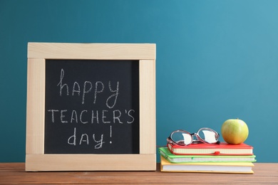 Photo of Little blackboard with inscription HAPPY TEACHER'S DAY, notebooks and eyeglasses on table