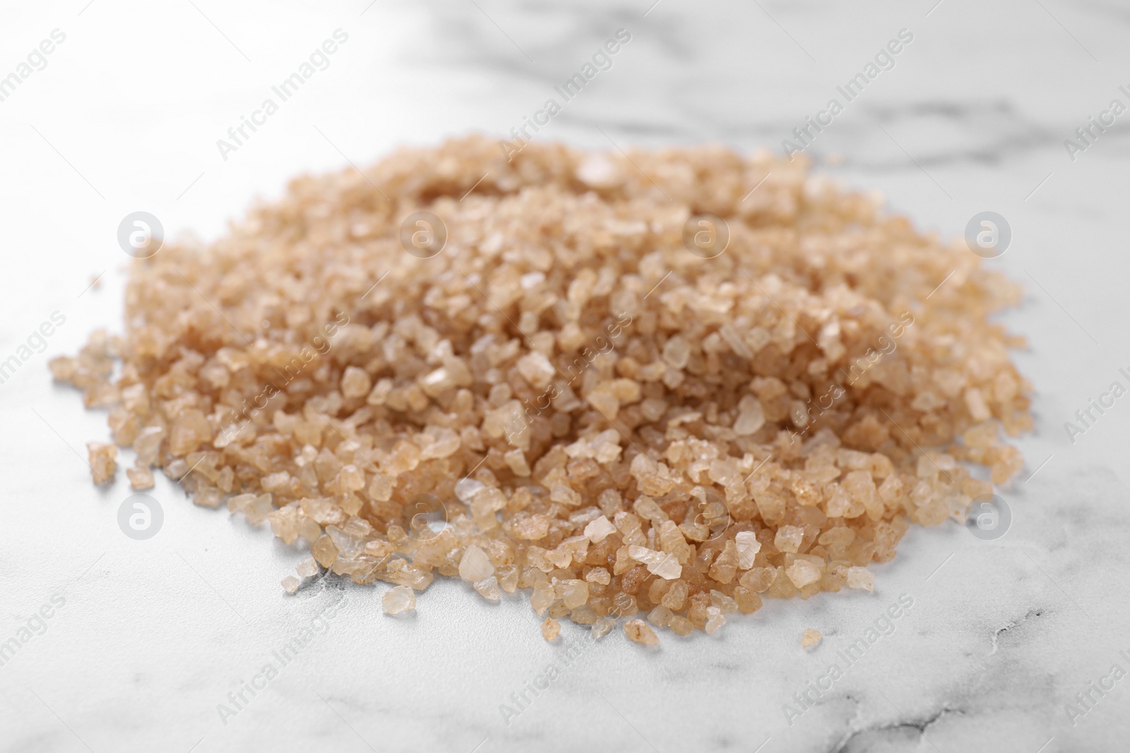 Photo of Pile of brown sea salt on white marble table, closeup. Spa treatment