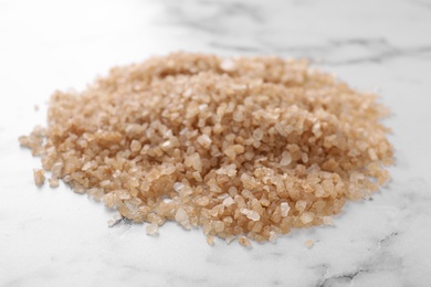 Photo of Pile of brown sea salt on white marble table, closeup. Spa treatment