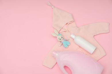 Photo of Bottles of laundry detergents, baby sweatshirt and toy bunny on pink background, flat lay. Space for text
