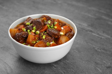 Delicious beef stew with carrots, green onions and potatoes on grey table, closeup. Space for text