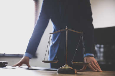 Male lawyer at table in office, focus on scales of justice