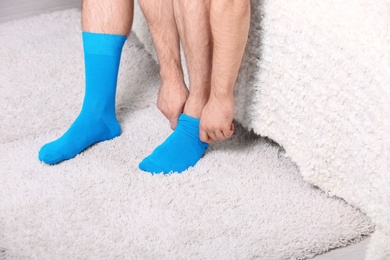 Photo of Man putting on stylish socks in bedroom, closeup