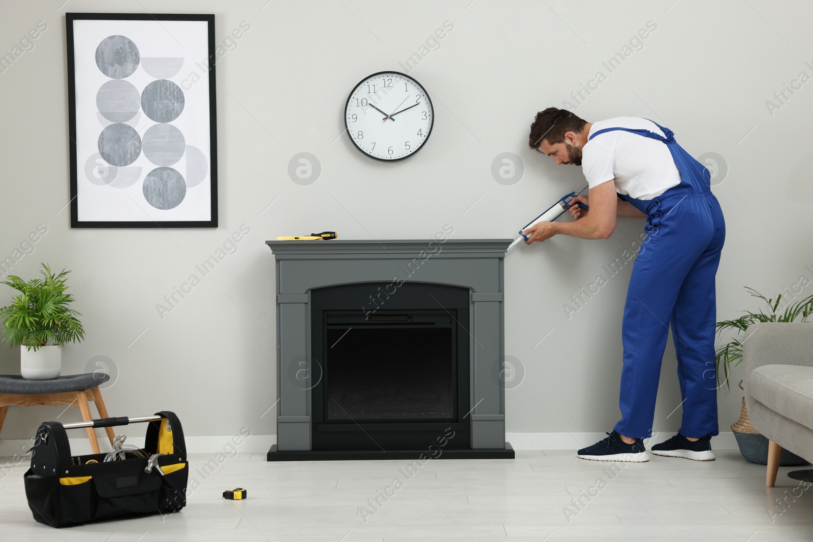 Photo of Professional technician sealing electric fireplace with caulk near white wall in room