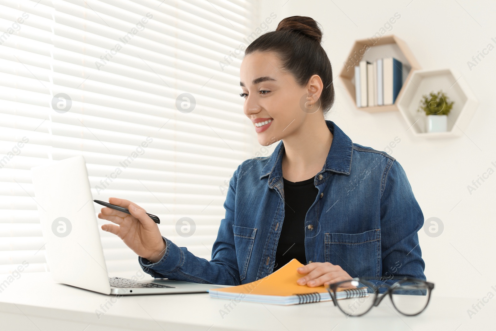 Photo of Home workplace. Happy woman working on laptop at white desk in room