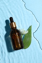 Photo of Bottle of cosmetic oil, green leaf and flower in water on light blue background, flat lay