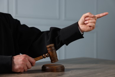 Judge with gavel pointing and sitting at wooden table indoors, closeup