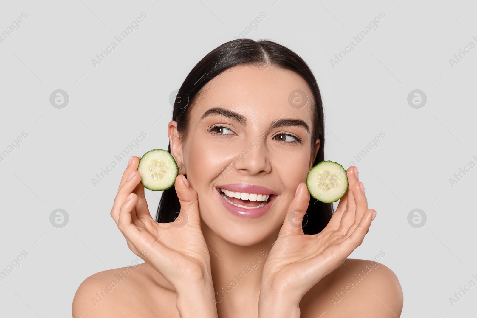 Photo of Woman holding pieces of cucumber on light grey background. Spa treatment