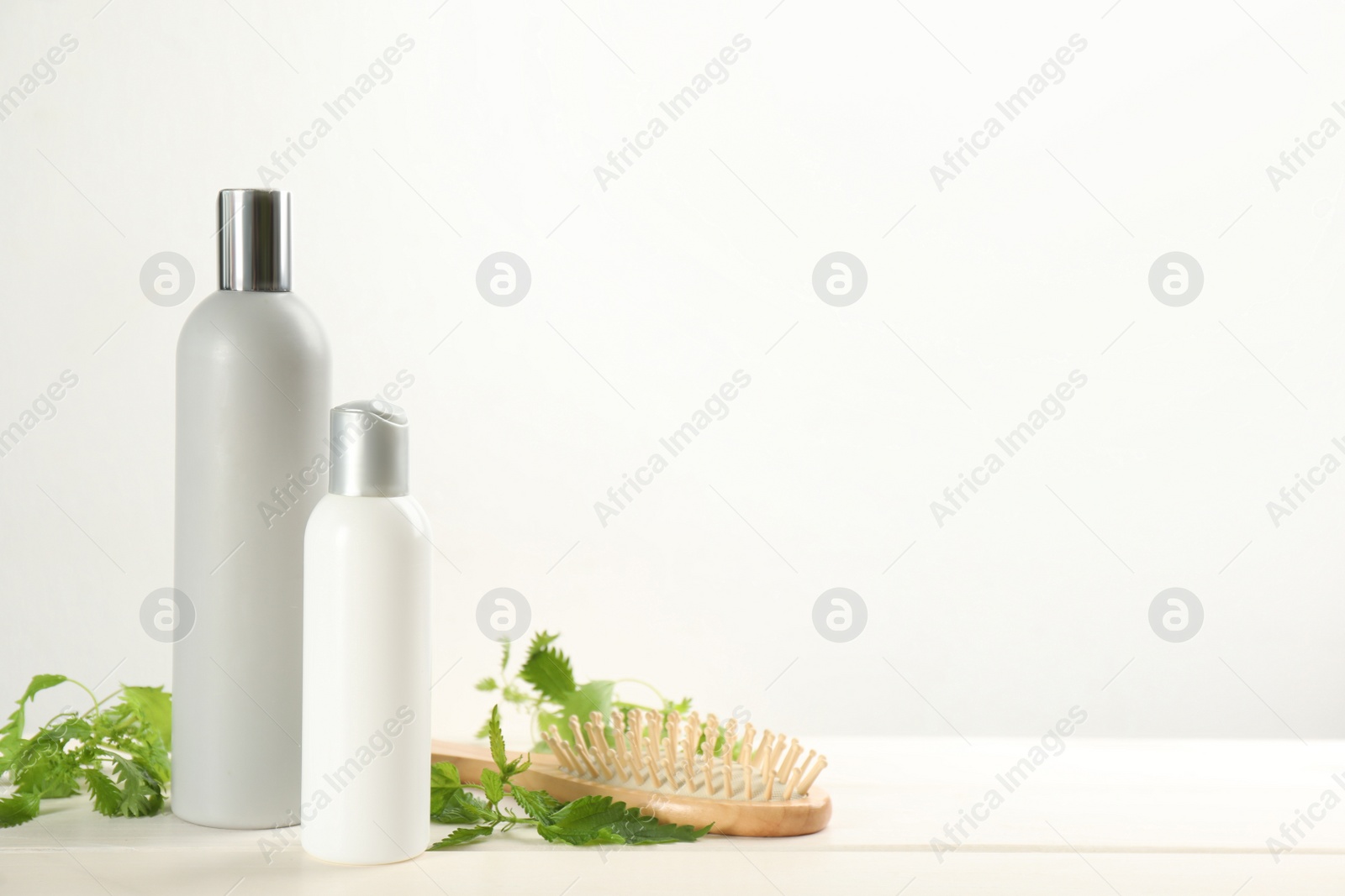 Photo of Stinging nettle, cosmetic products and brush on white wooden background, space for text. Natural hair care