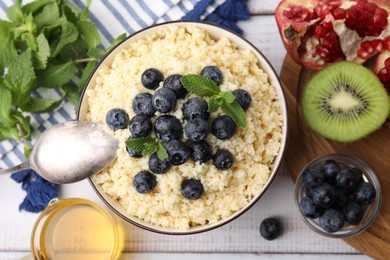 Photo of Bowl of tasty couscous with blueberries and mint served on white table, flat lay