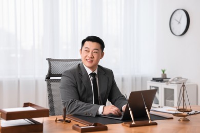 Happy notary working with laptop at wooden table in office