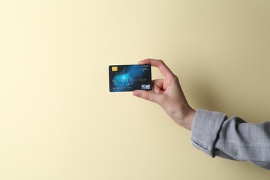 Woman holding credit card on beige background, closeup