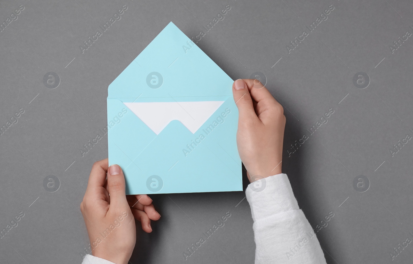 Photo of Woman holding letter envelope with card at grey table, top view