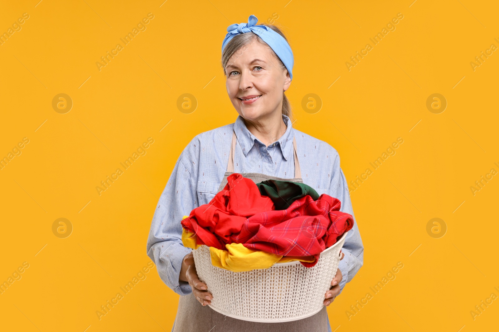 Photo of Happy housewife with basket full of laundry on orange background