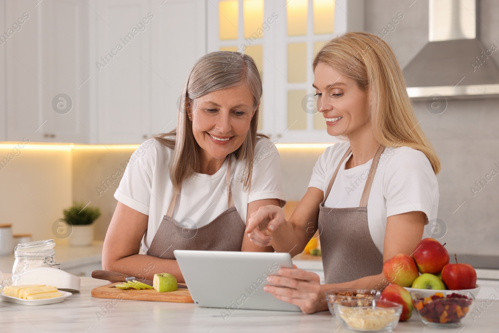 Photo of Happy mature mother and her daughter using tablet while cooking in kitchen